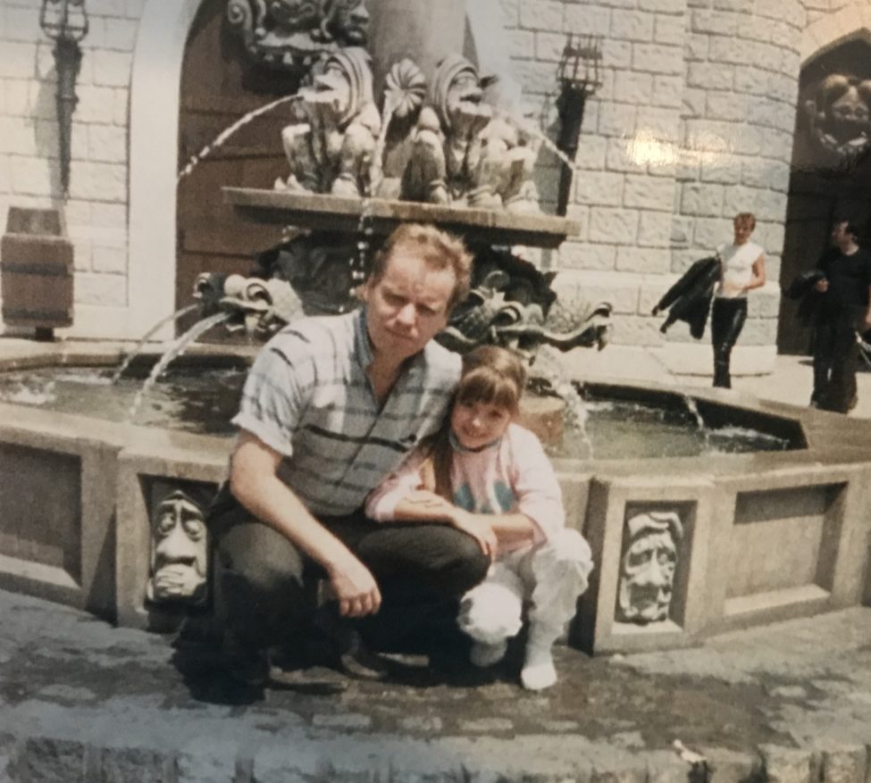 Father and Daughter crouching in front of a fountain