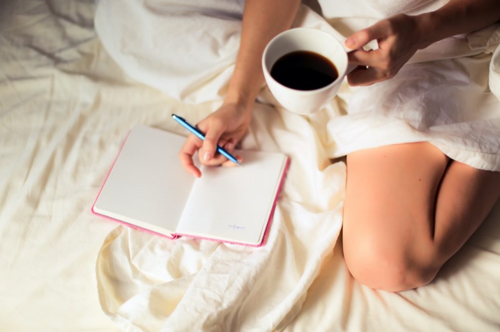 womans lap holding coffee writing in a journal positive affirmations 