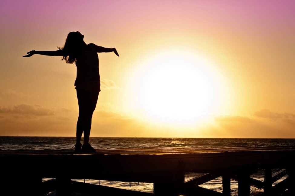 woman with arms outstretched in front of a sunset