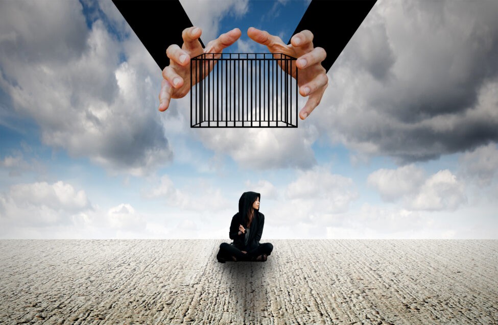 woman sitting on the ground with a hand about to drop a cage on her from above limiting beliefs