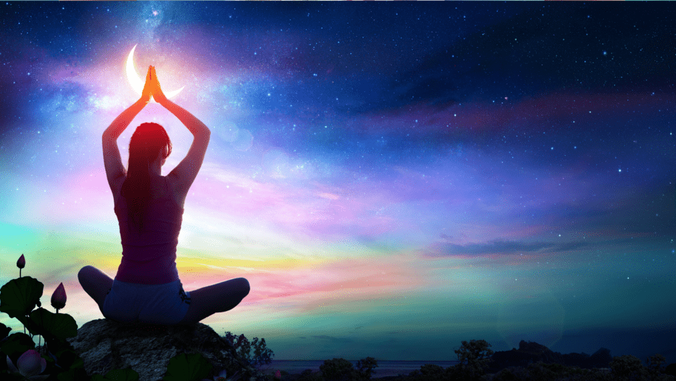 silhouette of person sitting in lotus position with colourful sky in background