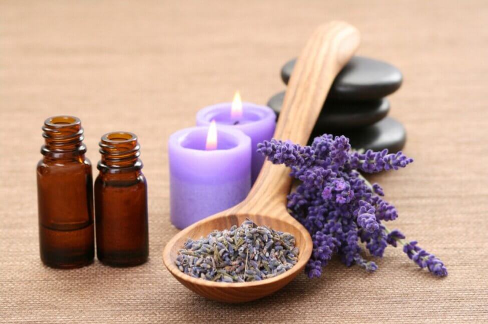 lavender in and around a wooden spoon with purple candles and essential oil bottles