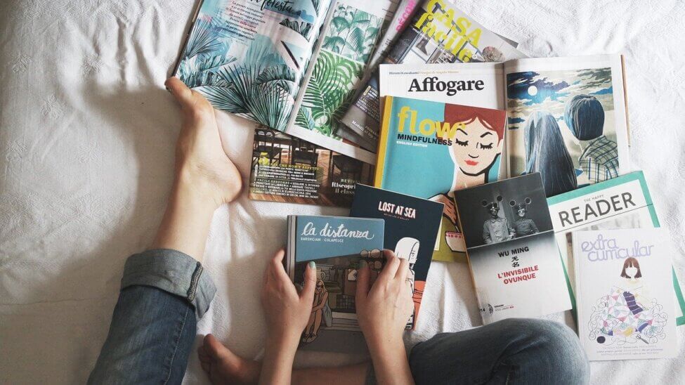 woman feet on a bed with books and magazines spread out